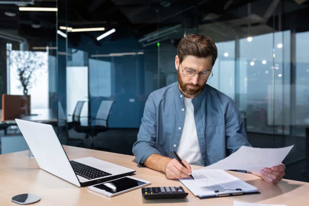 A young professional man in a blue shirt doing work at his office desk