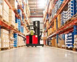 Worker in forklift-truck loading packed goods in huge distribution warehouse with high shelves.