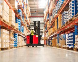 Distribution Services Worker in forklift-truck loading packed goods in huge distribution warehouse with high shelves.