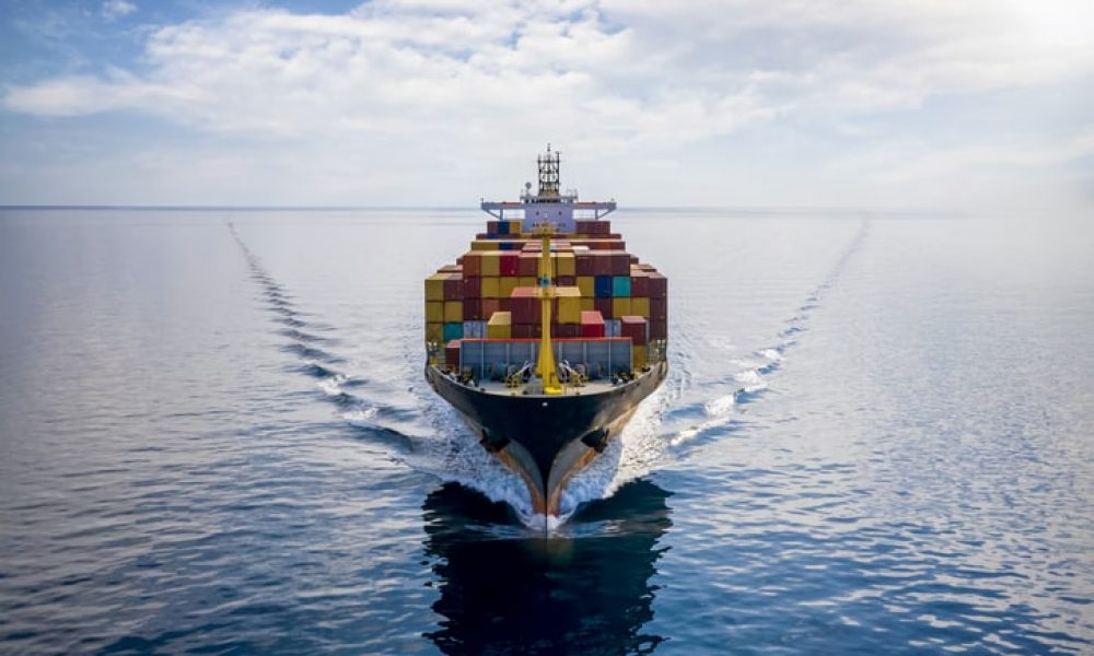 Aerial front view of a loaded container cargo vessel traveling over calm ocean